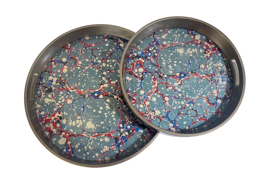 Deux plateaux ronds en métal gris avec un motif de papier marbré bleu ciel, rouge, bleu foncé et blanc moucheté.